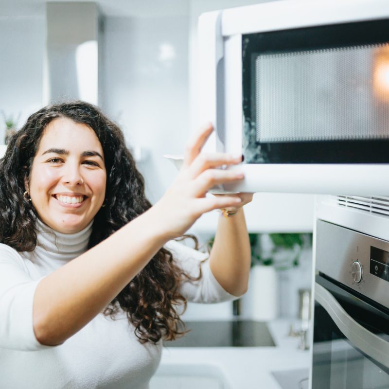 Young plus size spanish woman cooking on a microwave at a modern kitchen